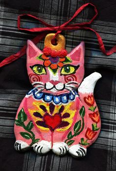 a painted cat ornament hanging from a red ribbon on a black and white plaid background