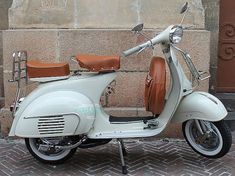 a white scooter parked next to a wall with brown leather seat covers on it