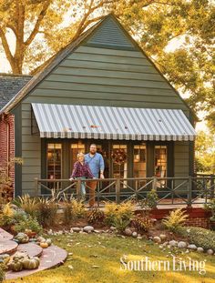 two people standing on the porch of a small house in front of trees and bushes