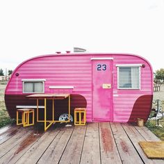 a pink trailer parked on top of a wooden deck next to a small table and chairs