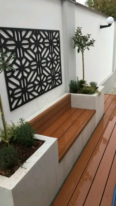 a wooden deck next to a white wall with a planter and tree on it