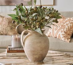 a vase filled with green leaves on top of a table next to a book and candle