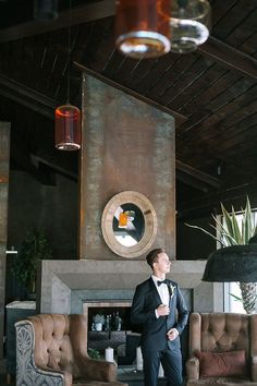 a man in a tuxedo standing next to a fire place and couches