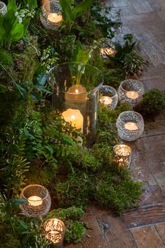 candles are lit in glass vases with moss growing on the ground next to them