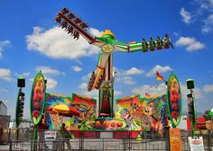 an amusement park ride with colorful rides and flags on the ground in front of a blue sky