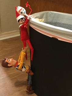 two elfs hanging from the side of a large trash can with water in it