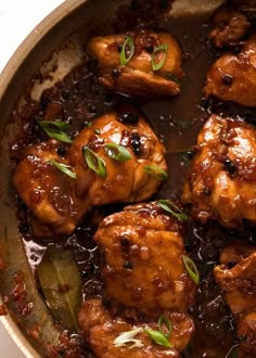 some chicken is cooking in a pan with sauce and green garnish on top