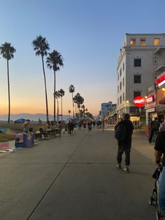 people are walking down the street in front of buildings and palm trees at sunset or dawn