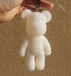 a hand holding a white teddy bear made out of tiny beads on a brown carpet