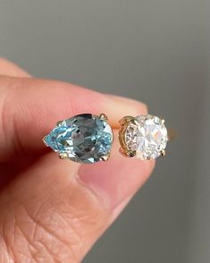 a pair of blue and white diamond earrings in someone's left hand, with the top one showing