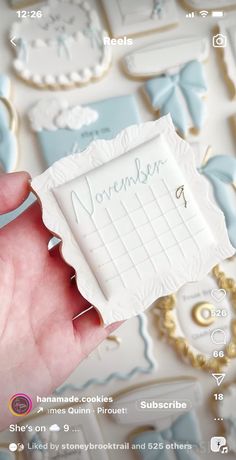 someone holding up a cookie in front of some cookies on a table with blue and white icing