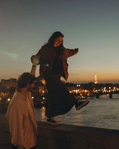 two people are standing on a ledge near the water