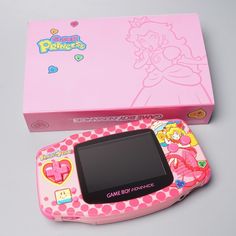 a pink game boy advance next to a pink box on a gray surface with an image of princess peach