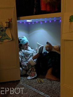 a child is sitting on the floor reading a book while wearing a hat and holding a teddy bear