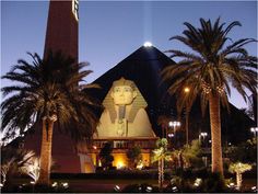 the egyptian pyramid is lit up at night with palm trees around it and lights on