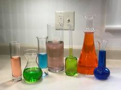 there are many different colored vases on the counter top, including one with liquid in it