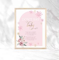 a pink and gold baby shower sign with flowers on it, against a marble background