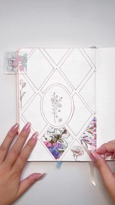 two hands holding an open notebook with floral designs on the pages and one hand pointing at it