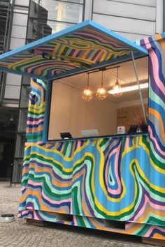 a colorfully painted food stand on the side of a street with lights hanging above it