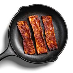 three pieces of bacon cooking in a frying pan on a white background, top view