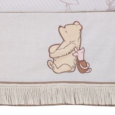 a baby bed with a teddy bear on it's back and fringe trim around the edges