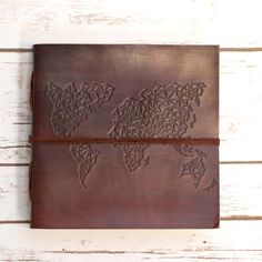 a brown leather journal with the world map on it, sitting on a white wooden surface