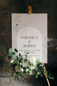 a wedding sign with flowers and greenery is displayed in front of an easel