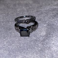 two black diamond rings sitting on top of a gray surface with sparkles around them