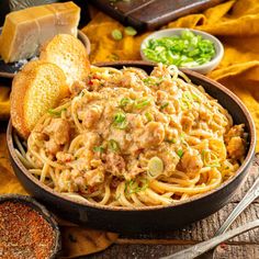 a bowl filled with pasta and meat sauce next to bread slices, green onions and seasonings