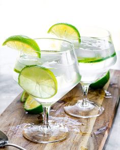 two glasses filled with water and limes on a cutting board