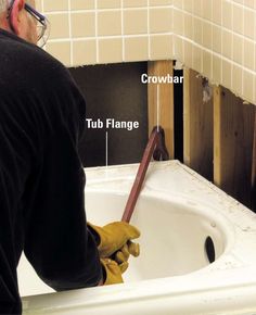 a man in black shirt and yellow gloves working on a white sink with wood framing around it