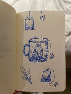 an open book with drawings on it and coffee mugs in the middle, sitting on a bed