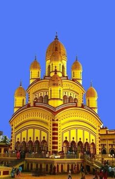 a large yellow building with many domes on it's sides and people walking around