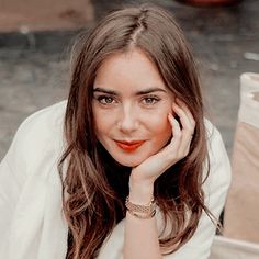 a woman sitting down with her hand on her chin and looking at the camera while wearing a white shirt