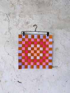 a piece of art hanging on the side of a wall with an orange and pink checkerboard pattern