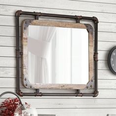 a mirror hanging on the side of a wall next to a vase with red flowers