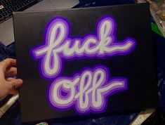 a person is painting the words f k off on a black box with purple and white paint