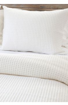 a white bed with two pillows on top of it and a wooden headboard in the background