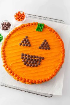 a cake decorated with an orange smiley face on top of a white paper towel next to some candies