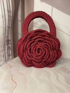 a red crocheted purse sitting on top of a white bed next to a pillow