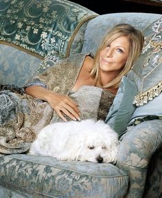 a woman laying on top of a blue couch next to a white dog in her lap