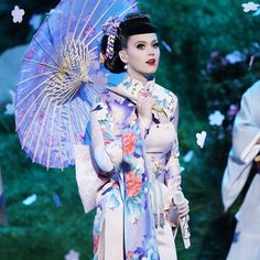 a woman in a kimono holding an umbrella and standing next to another woman with flowers on her head