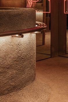 a close up of a metal object on the ground near a wall with neon lights behind it