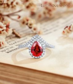 a red diamond ring sitting on top of a piece of paper with flowers in the background