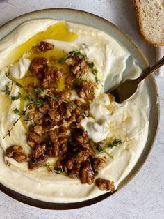 a bowl filled with mashed potatoes topped with walnuts and herbs next to a slice of bread