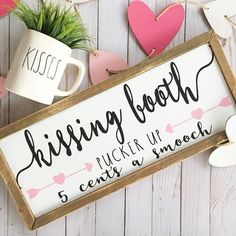 a wooden sign that says kissing booth with hearts around it and two mugs next to it