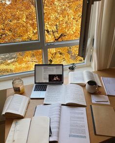 an open laptop computer sitting on top of a wooden table next to books and papers