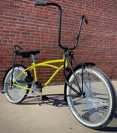 a yellow bicycle parked in front of a brick wall with the wheel turned upside down