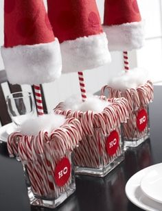 candy canes with santa hats on them are sitting in glass holders at the table