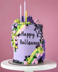 a birthday cake decorated with candles and decorations on top of a white pedestal in front of a pink wall